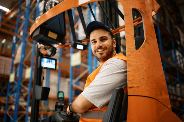 istock Happy male worker driving forklift at distribution warehouse and looking at camera. 1396631516