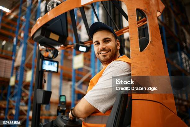 Happy Male Worker Driving Forklift At Distribution Warehouse And Looking At Camera Stock Photo - Download Image Now