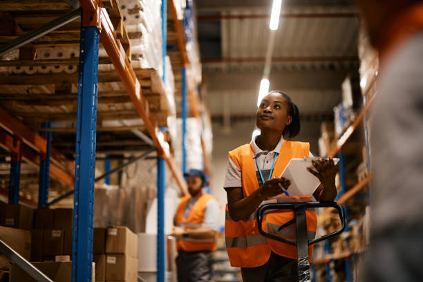 trabajadora negra del almacén revisando el stock de mercancía en el trastero. - los trabajadores de almacén fotografías e imágenes de stock