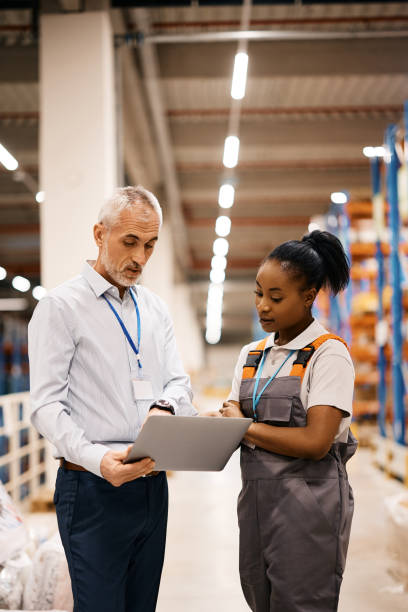 istock Mature warehouse manager and black female worker cooperating while working laptop. 1396632803