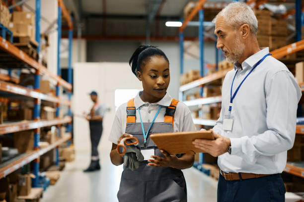 istock Mature foreman and black female worker using touchpad at distribution warehouse. 1396633136