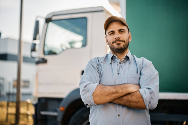 Truck driver standing with arms crossed in front of his truck and looking at camera. stock photo