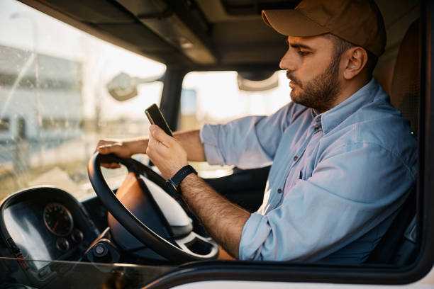 widok z boku kierowcy ciężarówki czytającego wiadomość tekstową na smartfonie podczas jazdy. - truck driver truck driver driving zdjęcia i obrazy z banku zdjęć