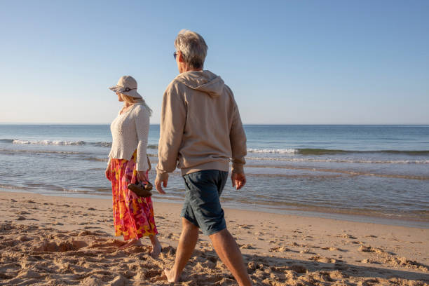 istock Mature couple walk, barefoot, down sandy beach 1396636588