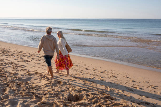 istock Mature couple walk, barefoot, down sandy beach 1396636754