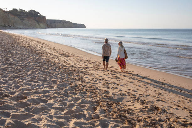 istock Mature couple walk, barefoot, down sandy beach 1396637307