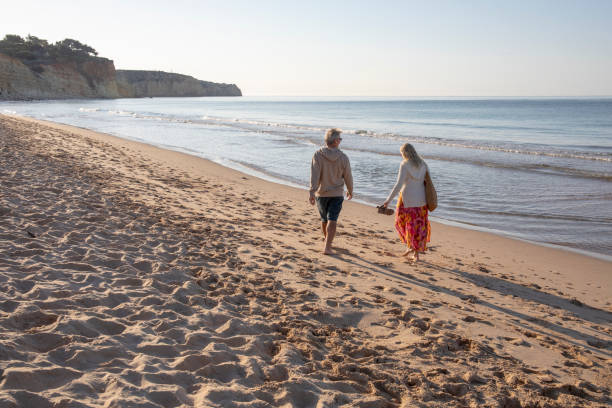 istock Mature couple walk, barefoot, down sandy beach 1396637308