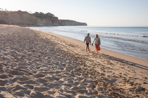 istock Mature couple walk, barefoot, down sandy beach 1396637330