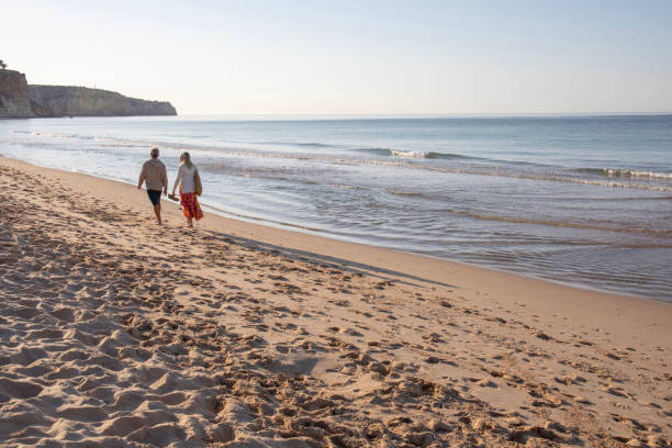 istock Mature couple walk, barefoot, down sandy beach 1396637365
