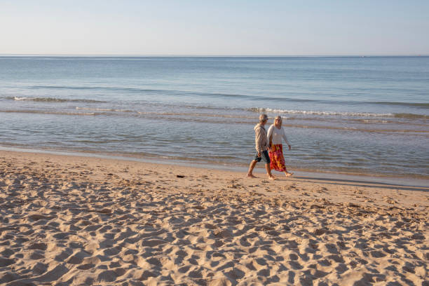 istock Mature couple walk, barefoot, down sandy beach 1396637427