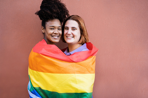 Happy women gay couple wearing rainbow flag outdoor - Love concept - Focus on faces