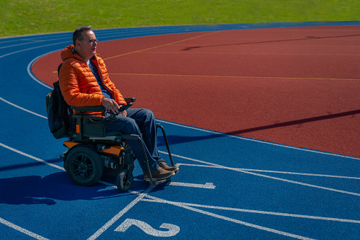 A disabled man in a motorized wheelchair nostalgically on a blue treadmill on a sports field.