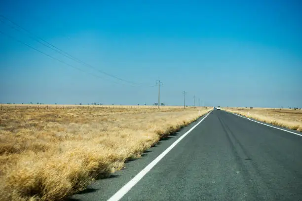 Long straight road near Corfield in rural Australia with dry grass and clear blue sky.
