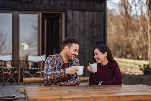 Beautiful couple drinking coffee, sitting in front of their wooden cottage.