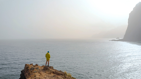 He stands on elevated rocky cliff, in Madeira