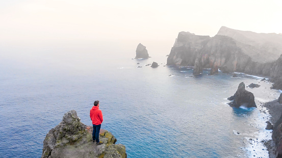 He stands on elevated rocky cliff, in Madeira