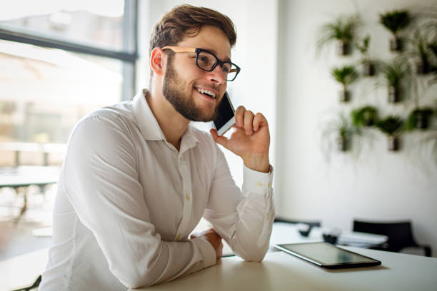 Smiling businessman sitting in cafe and using tablet while talking by his phone Smiling young businessman sitting in cafe and using tablet while talking by his phone restaurant labor union stock pictures, royalty-free photos & images