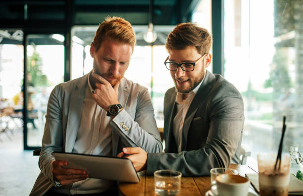 istock Happy young business people drinking coffee and working with tablet at cafe. 1396646679