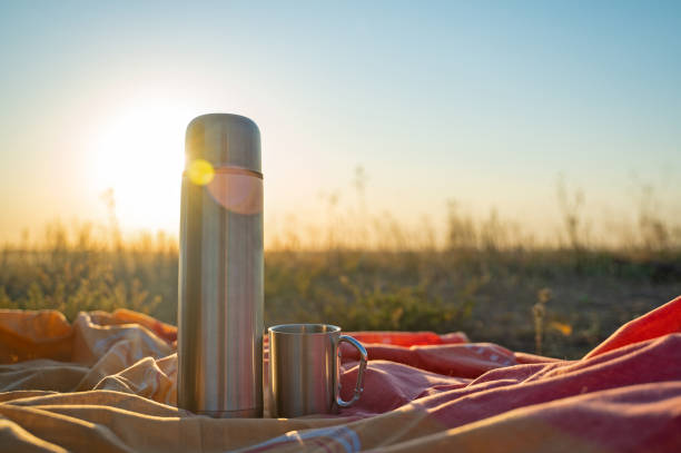 istock Thermos and camping cup on a bedspread against the backdrop of sunset or sunrise 1396648500
