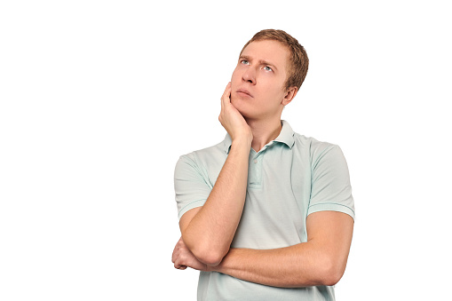 Thoughtful guy in mint T-shirt looking to left isolated on white background. Pensive young man thinking, guy putting hand to his head and looks to left, philosophical reflection concept