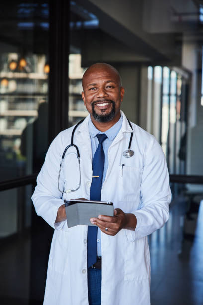 medico maschio maturo sorridente che usa un tablet in un corridoio dell'ospedale - doctor male doctor mature men portrait foto e immagini stock