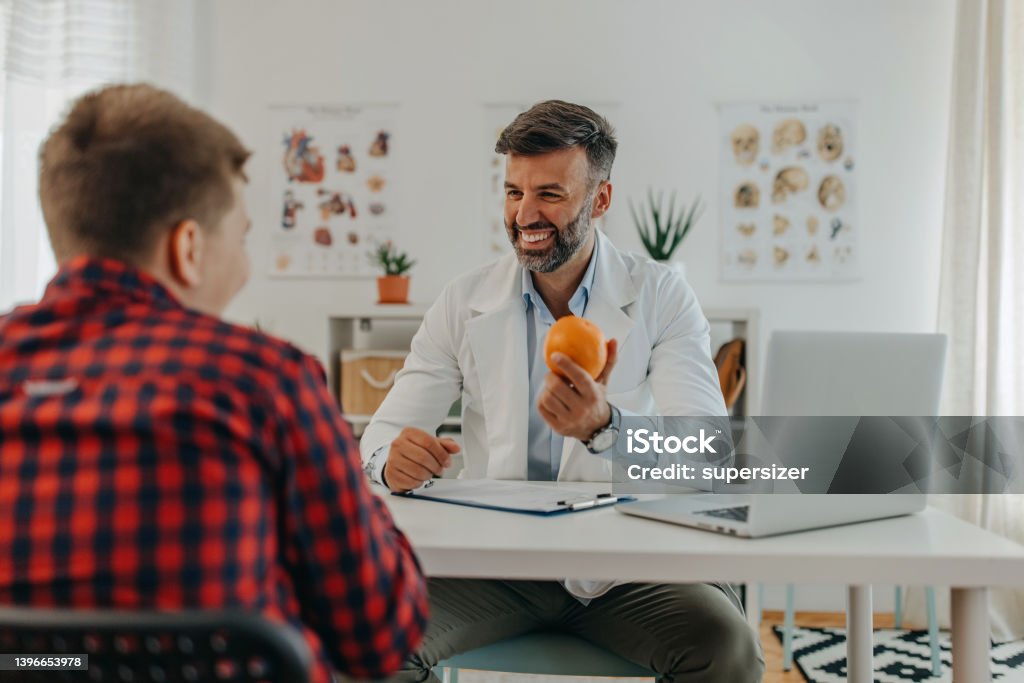 Ornage a day One mid adult doctor talking to teenage patient about eating healthy food Nutritionist Stock Photo