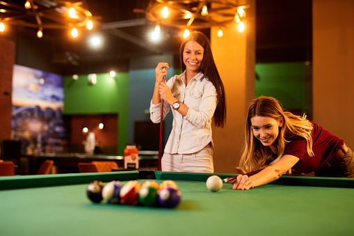 Two female friends enjoying a game of pool in a local pool hall