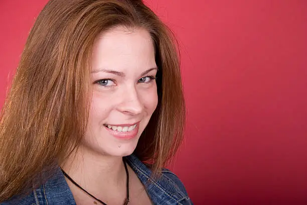 A young adult(girl) smiling on a red background.