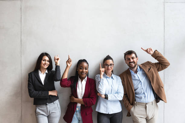 Group of young happy successful business team people pointing finger up and smiling. Freelancers or exchange students showing above and smile looking at the camera. Group of young happy successful business team people pointing finger up and smiling. Freelancers or exchange students showing above and smile looking at the camera. expatriate photos stock pictures, royalty-free photos & images