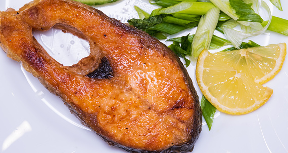 fried juicy trout steak with lemon and green onions on a white plate