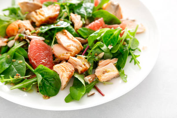 Stock photo showing close-up, elevated view of healthy smoked salmon, avocado and grapefruit salad with mixed lettuce leaves and a garnish of edible flower petals.