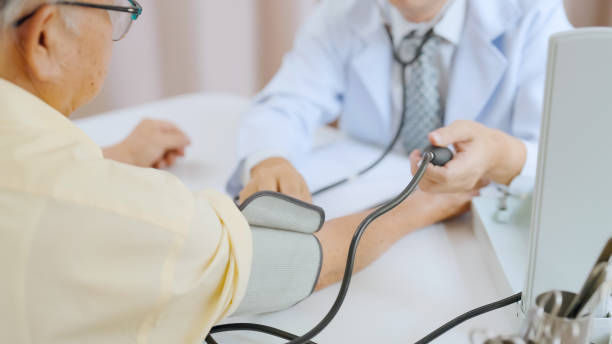 patient âgé asiatique ayant un examen médical avec un médecin à l’hôpital. un médecin ajuste un tensiomètre sur un homme âgé aux cheveux gris - blood pressure gauge medical exam healthcare and medicine equipment photos et images de collection