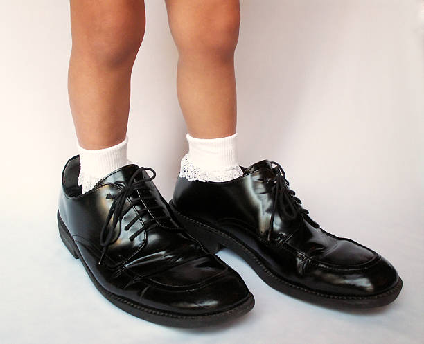 A small child is wearing daddy's shoes for dress up stock photo