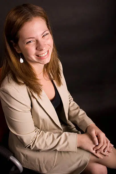 A young adult businesswoman sitting in a chair, looking up at the camera and smiling.