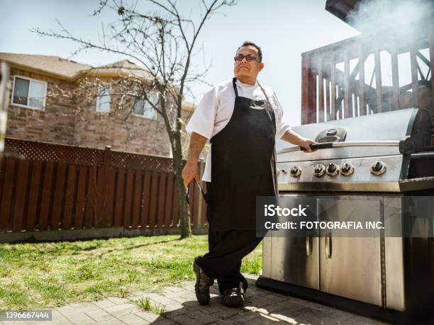 Mature Latin Chef Posing By The Backyard Bbq Stock Photo - Download Image Now - Barbecue Grill, Expertise, Chef