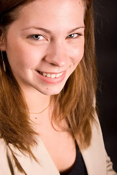A young adult business woman wearing a suit, smiling at the camera.