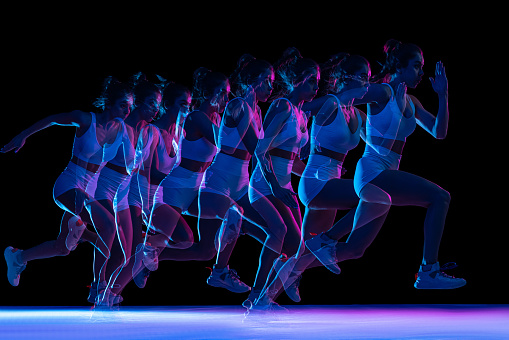 Muscular healthy woman running. Caucasian female runner in sportswear sprinting on black background.