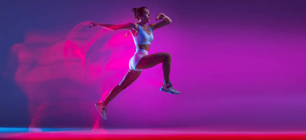 volantino con atleta professionista, runner training isolato su sfondo blu studio in luce neon rosa mista. sport, movimento e concetto di azione. - women action jumping running foto e immagini stock