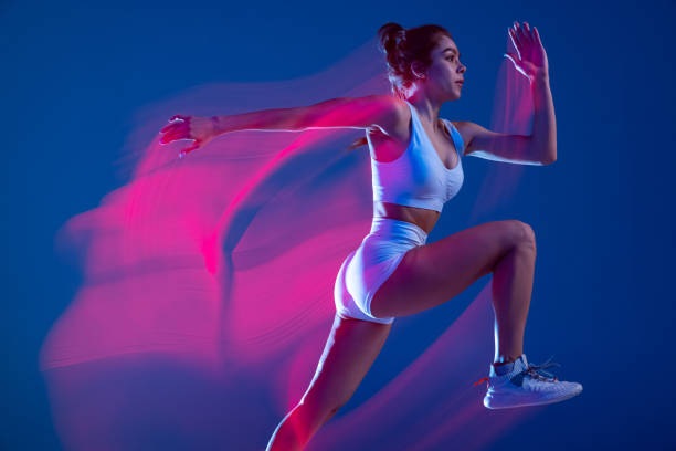 istock Profile view of female athlete, runner training isolated on blue studio background in mixed pink neon light. Healthy lifestyle, sport, motion and action concept. 1396668584