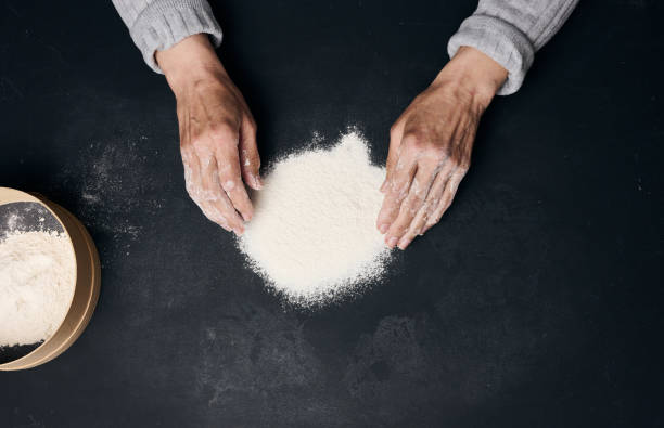 istock White wheat flour on a black table and two female hands, top view 1396669032