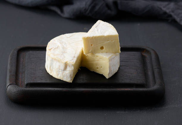 istock round brie cheese on brown wooden cutting board, black background 1396669203