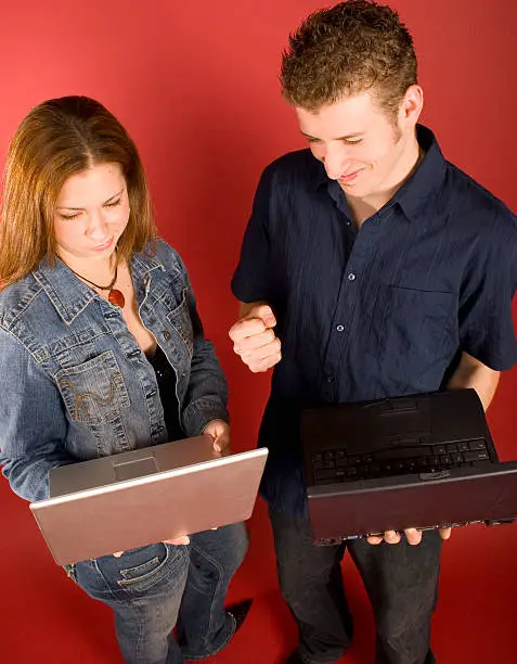 Young adults(male and female) working with laptops.  Male is excited about success, female is smug, considering.