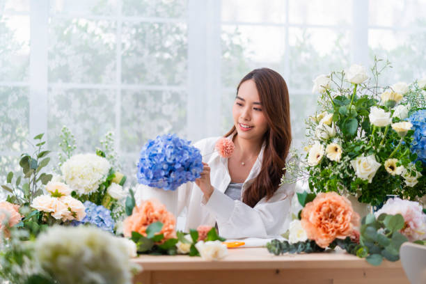 Small business. Asia Female florist smile arranging flowers in floral shop. Flower design store. happiness smiling young lady making flower vase for customers, preparing flower work from home business stock photo