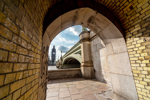 Looking across to Westminster Palace and Big Ben under renovation,summer sunlight shining into the brick tunnel that runs under the iconic bridge,crossing the River Thames.