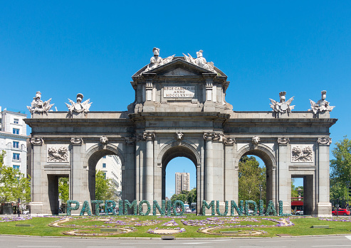 Madrid, Spain - 24th April 2022. The Puerta de Alcalá, in Plaza de la Independencia, with a Patrimonio Mundial sign in front to celebrate the adjacent Retiro Park being granted UNESCO World Heritage Site status in 2021. The city gate was designed by Francesco Sabatini, with sculptural details by  Francisco Gutiérrez and Roberto Michel, and was completed in 1778.