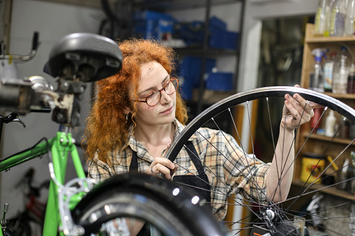 Young woman working in a bicycle repair shop. About 25 years old, Caucasian redhead.