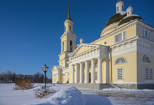 Majestic stone Orthodox church with a bell tower, white columns, yellow domes in the historical center of Nevyansk (Urals, Russia). Winter sunny day, blue sky, a lot of white snow in snowdrifts