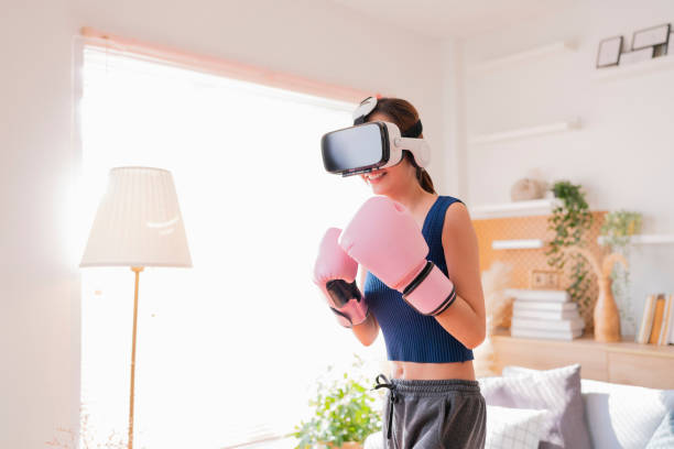 Virtual Metaverse Augmented Reality asian female adult working out boxing in VR headset aerobic training for boxing punch in virtual reality at living room home interior background stock photo
