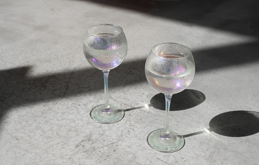 Two wine glasses with water on light concrete background with hard shadows.