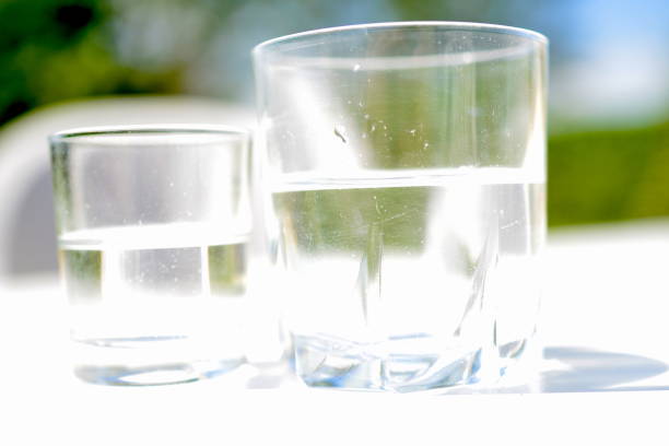 Climate change: is also water shortage. Drinking water, spring water 2 glass cups half filled, They got all 50% full. Concept of honesty. Little focus depth image. Blurred image like  the view of a drunk person concept club soda stock pictures, royalty-free photos & images